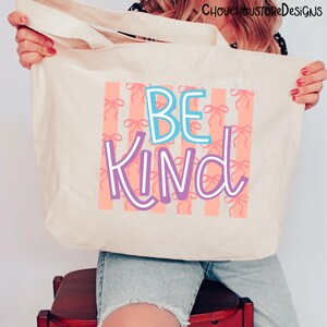 以下が含まれることがあります： 「BE KIND」の文字が青と紫で描かれたベージュのトートバッグ。背景には、ピンクのリボンがピーチ色のストライプに配置されています。バッグにはクリーム色のハンドルが付いています。