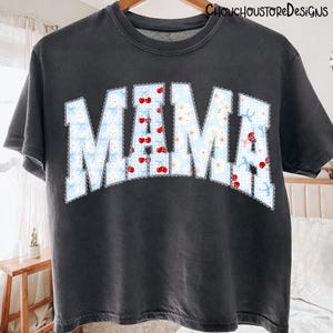 May include: Dark gray t-shirt with the word "MAMA" in a light blue floral and cherry design. The letters are outlined with a white scalloped edge. The shirt has a vintage, worn look and the text "CHOUCHOUSTOREDESIGNS" is printed at the top.