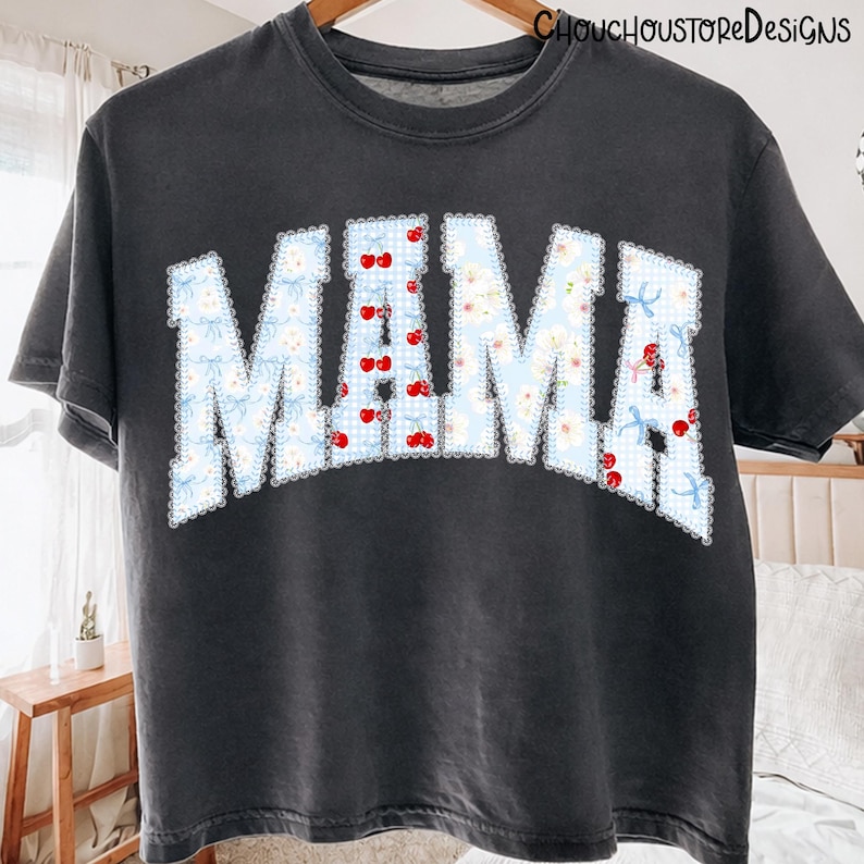 May include: Dark gray t-shirt with the word "MAMA" in a light blue floral and cherry design. The letters are outlined with a white scalloped edge. The shirt has a vintage, worn look and the text "CHOUCHOUSTOREDESIGNS" is printed at the top.