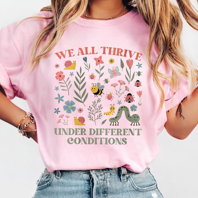 Peut inclure: T-shirt rose clair avec l'inscription "WE ALL THRIVE UNDER DIFFERENT CONDITIONS". Le motif comprend des fleurs et des insectes color&eacute;s, tels que des escargots, des abeilles, des papillons et des coccinelles. Le motif est imprim&eacute; sur le devant.