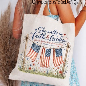 May include: Cream-colored tote bag featuring the text "She walks in faith & freedom" with American flags and floral accents. The design includes the scripture 2 Corinthians 3:17. The bag has a patriotic theme.