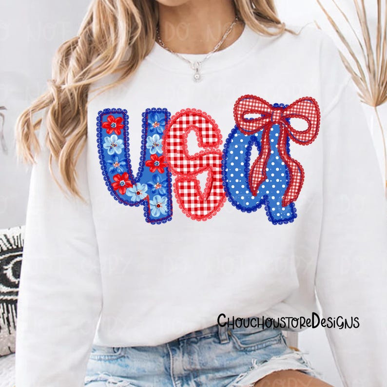 May include: White long-sleeved sweatshirt with a patriotic "USA" design. The letters are decorated with blue floral patterns, red gingham, and blue polka dots. The design includes a red gingham bow. The text "CHOUCHOUSTOREDESIGNS" is printed on the bottom right.