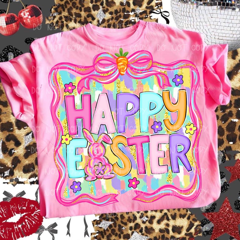 May include: Pink t-shirt with a colorful "Happy Easter" graphic. The design features a bunny, flowers, and a bow with a carrot. The text is in various colors, including pink, blue, and orange. A festive Easter-themed apparel item.