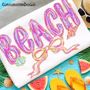 May include: White beach towel with the word "BEACH" in large, bubble letters. The letters are pink and purple with black polka dots and gold trim. A bow and seashells are also featured. The towel is surrounded by beach-themed accessories.