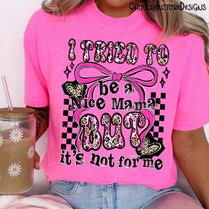 May include: Bright pink t-shirt with the text "I TRIED TO be a Nice Mama BUT it's not for me." The text features a leopard print design and is accented with a pink bow and black and white checkered pattern.