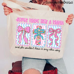 May include: Beige tote bag with the text "JESUS MADE HER A MAMA" and "and she wouldn't have it any other way." The design features three decorative elements: two bows and a cross, all in pink, blue, and floral patterns.