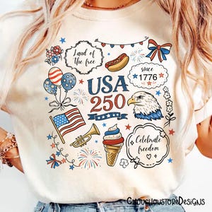 Puede incluir: Camiseta color crema con un dise&ntilde;o patri&oacute;tico que presenta el texto "USA 250" y varias ilustraciones. Incluye una bandera estadounidense, un &aacute;guila, fuegos artificiales y un helado. Tambi&eacute;n est&aacute; presente la frase "Land of the free".