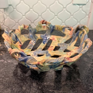 May include: A handcrafted ceramic bowl with a unique woven design. The bowl features a blend of colors, including blue, yellow, and red, creating a vibrant and artistic appearance. The bowl is suitable for decorative or functional use.