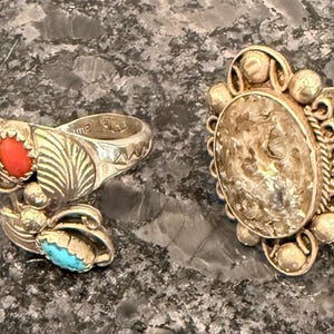 May include: Four silver rings with unique designs. One ring features a turquoise-filled horseshoe, another has a red stone and turquoise accents, a third has a large oval stone, and the last has colorful gemstones.