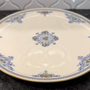 May include: Cream-colored ceramic serving platter with a gold rim and ornate blue, yellow, and red floral designs. The center features a similar medallion design. A decorative piece for serving food.