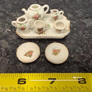 May include: A miniature porcelain tea set with a floral design. The set includes a teapot, creamer, sugar bowl, two teacups, and two saucers. The set is on a white tray with a gold trim.