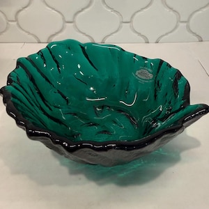 May include: A handcrafted, leaf-shaped glass bowl in shades of teal and black. The bowl features a textured surface with dark, wavy lines and a black rim. The label reads "Blenco Handcraft".