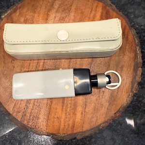 May include: A light gray and black keychain with a matching case. The keychain has a rectangular body with a black end and a silver ring. The case is a light cream color with a button closure.