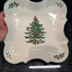 May include: A square, cream-colored ceramic serving dish with scalloped edges and a thin green rim. The center features a decorated Christmas tree with presents underneath. Holly and mistletoe sprigs are painted in the four corners of the dish.