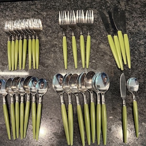 May include: A flatware set consisting of stainless steel forks, spoons, and knives with light green plastic handles. The collection includes various sizes of forks and spoons, along with several dinner knives and a small butter knife.