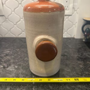 May include: A white ceramic jar with a brown lid and a brown knob. The jar has a rustic, handmade look.