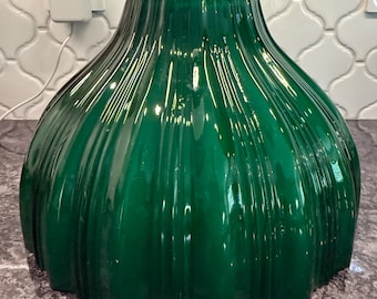 May include: A deep emerald green glass lamp shade featuring a wide, bell-shaped silhouette with vertical fluted ridges. The translucent glass has a glossy finish and a circular opening at the top, designed to fit onto a standard light fixture.
