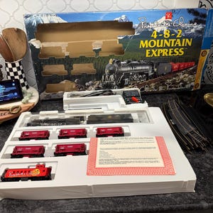 May include: A boxed model train set, "Children's Choice 4-8-2 Mountain Express." The set includes a black locomotive, red train cars, and track pieces. The box features a mountain scene and train illustration.