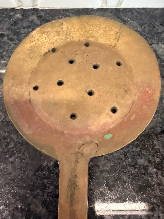 A 20.5" hammered copper skimmer spoon formed from a single piece of metal — the kind of heirloom-quality hand-forged utensil you'd find in a French farmhouse kitchen or a museum of craft.