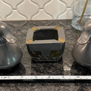 May include: Two pewter ducks with gold accents and a square pewter ashtray with gold accents. The ashtray has a square opening in the center.