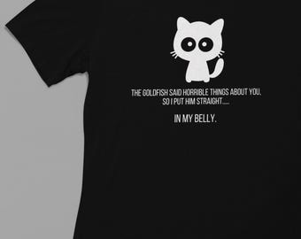 Pode incluir: Camiseta preta com um gato de desenho animado branco e o texto "THE GOLDFISH SAID HORRIBLE THINGS ABOUT YOU, SO I PUT HIM STRAIGHT..... IN MY BELLY."