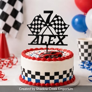 May include: A black cake topper featuring the number 7, two crossed checkered racing flags, and the name ALEX in capital letters. The topper is placed on a white cake with a checkered pattern border, red frosting, and a red toy race car.