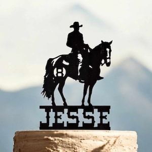 May include: Black silhouette of a cowboy riding a horse with the name "JESSE" underneath. The horse has a letter "B" on its side.