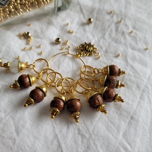 Könnte beinhalten: Ein goldener Strickring mit einem Sonnenanhänger und sechs Holzperlen mit goldenen Akzenten.