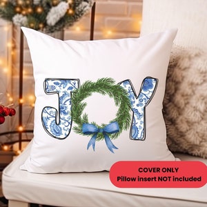 May include: White pillow cover with the word "JOY" in blue floral print letters. The "O" is a green wreath with a blue bow. The text "COVER ONLY Pillow insert NOT included" is in a red rectangle.