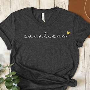 May include: A dark gray t-shirt with the word "cavaliers" written in white script with a small yellow heart to the right of the word.