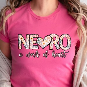 May include: Pink t-shirt with a floral design that says "NERO a work of heart".