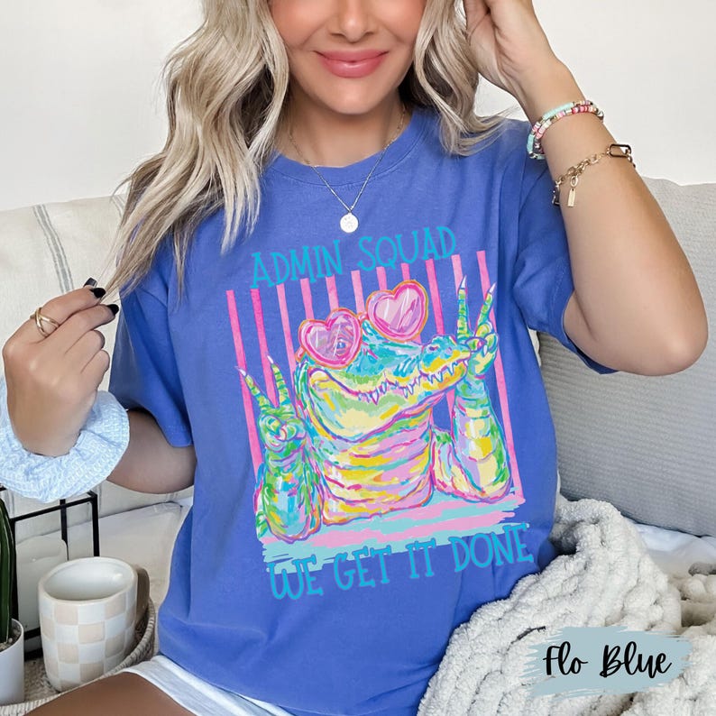 K&ouml;nnte beinhalten: Ein blaues T-Shirt mit einer bunten Grafik eines Krokodils, das eine herzf&ouml;rmige Sonnenbrille tr&auml;gt und mit beiden H&auml;nden das Friedenszeichen zeigt. Der Text ADMIN SQUAD steht dar&uuml;ber und WE GET IT DONE steht in T&uuml;rkis darunter.