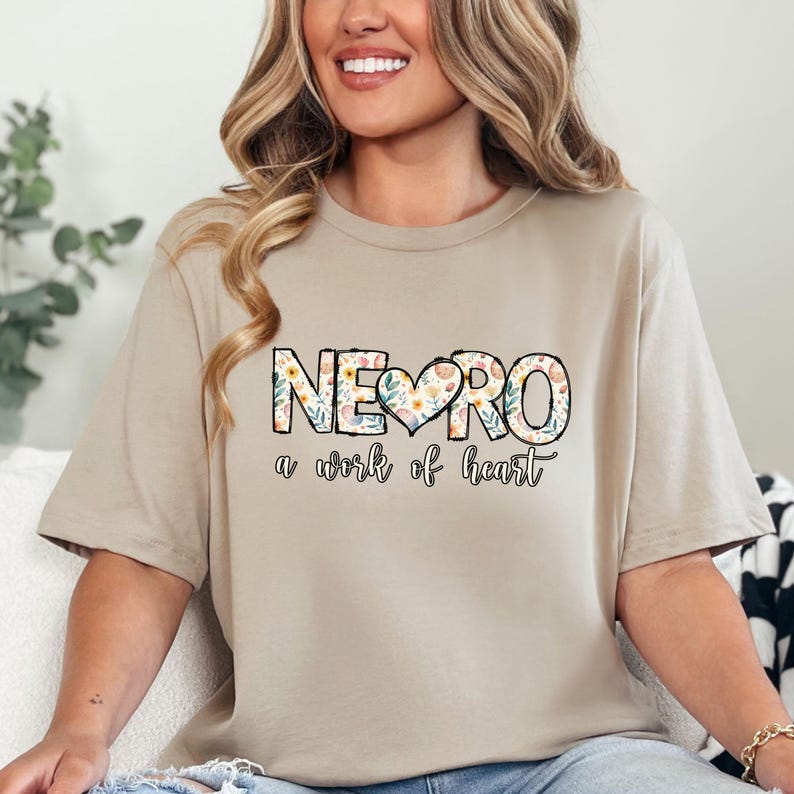 May include: A beige t-shirt with a floral design that spells out "NEURO" with a heart in the middle. The text below the design reads "a work of heart".
