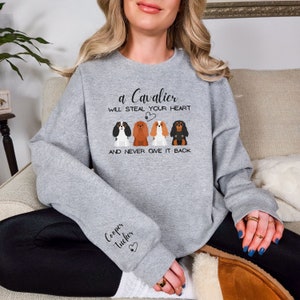 May include: Gray sweatshirt with a graphic of three Cavalier King Charles Spaniels and the text "a Cavalier will steal your heart and never give it back". The sleeve has the text "Cooper Tucker" with a heart.