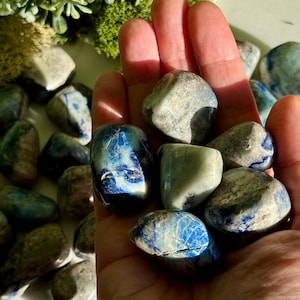 May include: A collection of tumbled stones in shades of blue, gray, and white. The stones are smooth and rounded, with a mix of solid and patterned surfaces. Some stones have striking blue veining.