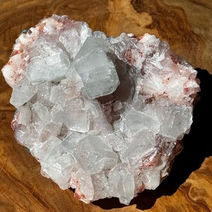 May include: A cluster of clear, white, and light green crystals with a reddish-brown base. The crystals are arranged in a random pattern and have a natural, rough texture.