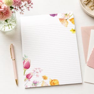 May include: A rectangular sheet of white lined stationery paper featuring watercolor floral illustrations in the top right and bottom left corners, showcasing pink tulips, yellow poppies, and small purple blossoms.
