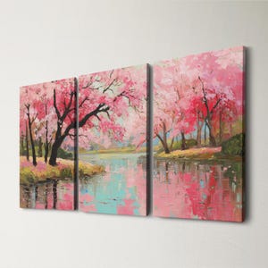 May include: A triptych canvas art piece depicting a serene landscape. The artwork features pink cherry blossom trees reflected in a calm body of water. The painting uses a palette of pink, blue, and green hues.