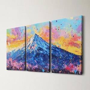 May include: A triptych canvas art piece featuring a mountain landscape. The artwork uses a vibrant palette of blues, yellows, pinks, and purples, with a splatter paint effect. The mountain peak is white, and the sky is a mix of colors.