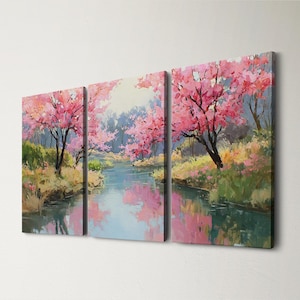 May include: A triptych canvas art print depicting a serene landscape. Pink flowering trees line a blue river, with their reflections mirrored in the water. The artwork features a blend of green, yellow, and blue hues, creating a tranquil scene.