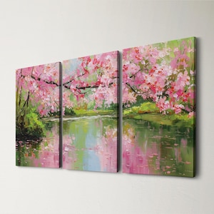 May include: A triptych canvas art piece depicting a serene landscape. The artwork features a body of water reflecting the pink blossoms of cherry trees. Green foliage and branches frame the scene, creating a tranquil and colorful composition.