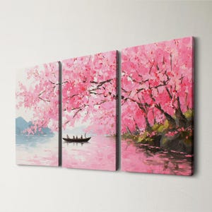May include: A triptych canvas art print depicting a serene landscape. The artwork features a pink cherry blossom scene with a boat on the water. The painting has a soft, impressionistic style with a focus on color and light.