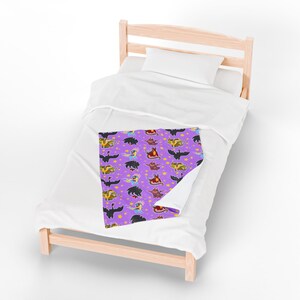 May include: A purple blanket with a repeating pattern of cartoon dragons and yellow stars. The dragons are in various colors, including black, yellow, red, and blue. The blanket is on a white bed.