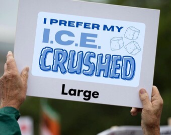 Può includere: Un cartello bianco tenuto in mano, con la scritta "I PREFER MY I.C.E. CRUSHED" in blu e la parola "Large" in nero. Il cartello presenta anche illustrazioni di cubetti di ghiaccio.