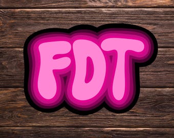 Könnte beinhalten: Rosa und schwarze 3D-Buchstaben, die "FDT" auf einem braunen Holzgrund buchstabieren.