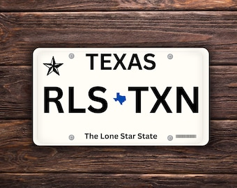 Può includere: Targa rettangolare bianca con testo nero e stella nera. La parola "TEXAS" è in alto, con "RLS TXN" sotto. Il testo "The Lone Star State" è in basso.