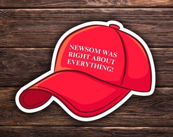 Può includere: Un adesivo a forma di cappellino da baseball rosso con la scritta bianca "NEWSOM WAS RIGHT ABOUT EVERYTHING!". Lo sfondo è in legno.