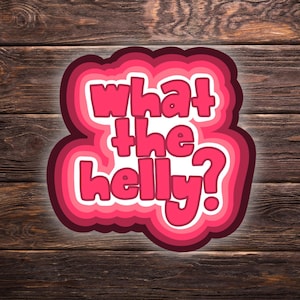 May include: A layered sticker with the phrase "What the Helly?" in a bubble font. The text is in white with a pink outline, set against a gradient of pink hues. The background is a wooden surface.