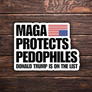 May include: A white sticker with black text that reads "MAGA PROTECTS PEDOPHILES" with an American flag graphic. The text "DONALD TRUMP IS ON THE LIST" is below the main text. The sticker is on a wooden background.