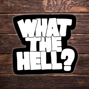 Può includere: Un adesivo nero con la scritta "WHAT THE HELL?" in grandi lettere bianche. Il testo è delineato in nero e posto su uno sfondo di legno.